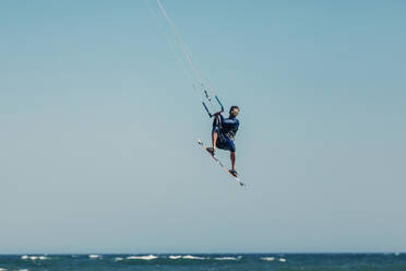 Älterer Mann beim Kiteboarding in der Luft über dem Meer an einem sonnigen Tag - DMGF00808
