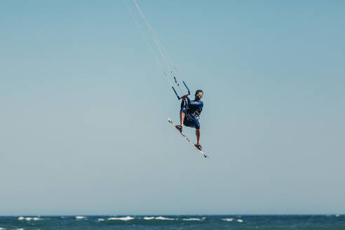 Mature man kiteboarding mid-air over sea on sunny day - DMGF00808