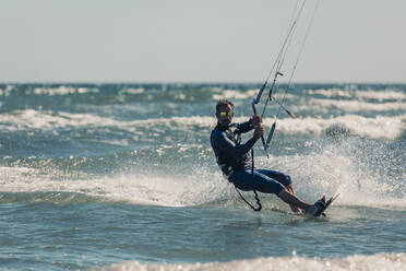 Man kiteboarding in sea splashing water on sunny day - DMGF00809