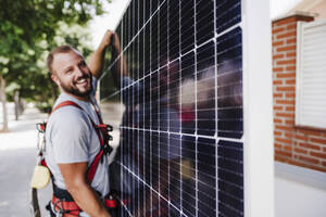 Lächelnder Techniker trägt schweres Solarpanel - EBBF05700
