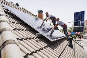 Craftsmen installing solar panels on rooftop of house - EBBF05705