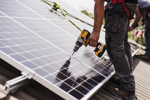 Elektriker bei der Installation eines Solarpanels auf dem Dach mit einem Elektrowerkzeug - EBBF05711