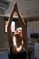 Mature woman doing stretching exercise under sunlight at home - VEGF05724