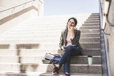 Happy transgender businesswoman talking on smart phone sitting on steps - UUF26884