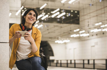 Smiling transgender businesswoman holding phone looking away at subway station - UUF26889