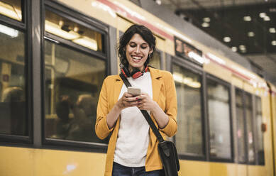 Happy businesswoman text messaging through mobile phone in front of train at subway station - UUF26892