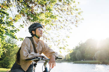 Nachdenkliche Frau mit Fahrrad im Park an einem sonnigen Tag - VPIF06715