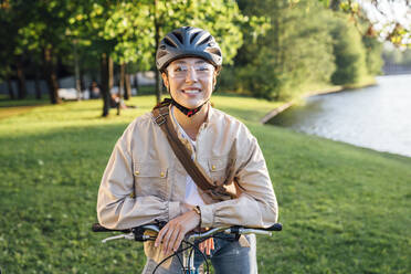 Lächelnde Frau mit Helm auf dem Fahrrad sitzend im Park - VPIF06718