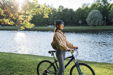 Lächelnde Frau mit Fahrrad an einem See im Park - VPIF06720