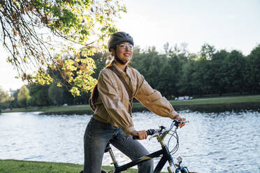 Smiling woman on bicycle by lake in park - VPIF06721