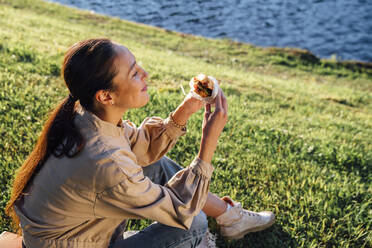 Frau isst Mittagessen auf Gras im Park an einem sonnigen Tag - VPIF06730