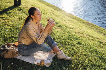 Frau sitzt im Gras beim Mittagessen im Park an einem sonnigen Tag - VPIF06731