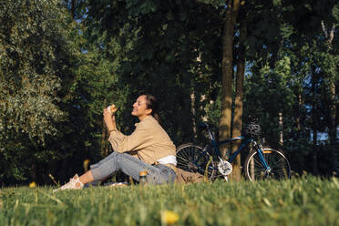 Glückliche Frau beim Mittagessen im Park an einem sonnigen Tag - VPIF06732