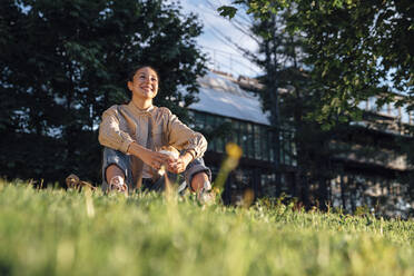 Happy woman sitting with food in hand at park - VPIF06733