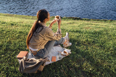 Woman having lunch sitting by lake at park - VPIF06734