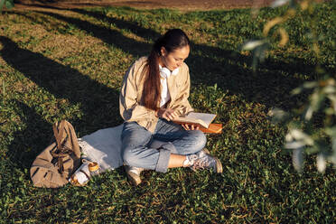 Woman sitting on grass reading book at park - VPIF06735