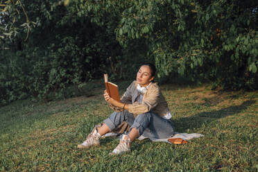 Woman reading book sitting on grass at park - VPIF06738