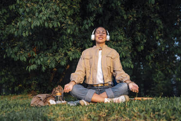 Woman listening music through wireless headphones at park - VPIF06740