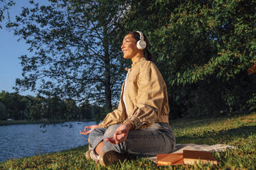 Smiling woman meditating on grass at park - VPIF06749