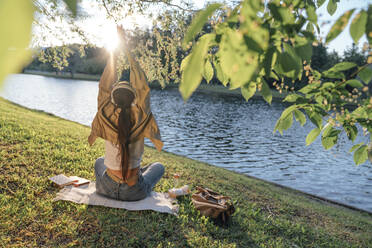 Woman with hands clasped by lake at park - VPIF06753