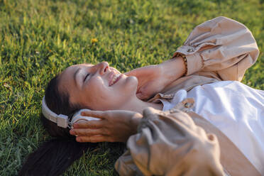 Smiling woman listening music through wireless headphones at park - VPIF06761