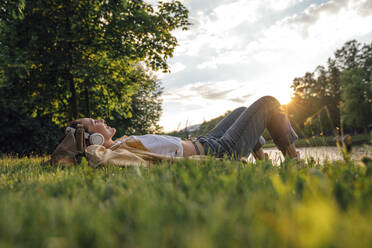 Woman with headphones lying on grass at park - VPIF06767