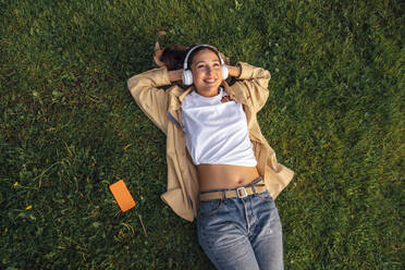 Smiling woman lying with hands behind head at park - VPIF06769