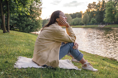 Frau sitzt mit Hand am Kinn am See im Park - VPIF06790