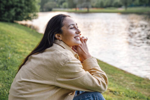 Lächelnde Frau sitzt am See im Park - VPIF06792