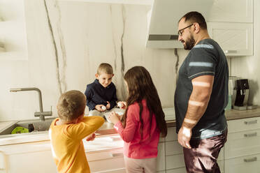 Vater mit Kindern bei der Zubereitung des Frühstücks in der Küche - OSF00392