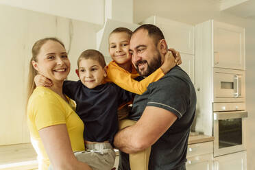 Lächelnde Eltern, die ihre Söhne in der Küche umarmen - OSF00408