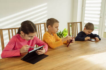 Glückliches Mädchen, das einen Tablet-PC benutzt und neben seinen Brüdern sitzt, die sich zu Hause mit Technik beschäftigen - OSF00422