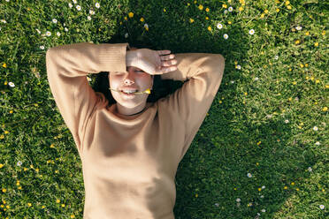 Lächelnde Frau mit geschlossenen Augen liegt im Gras und genießt den sonnigen Tag - OMIF00963