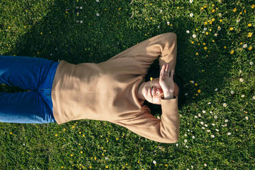 Young woman lying with hand covering eyes on grass at park - OMIF00964