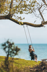 Mature woman swinging in front of sea - OMIF00975