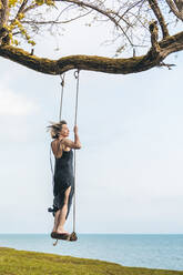 Mature woman standing on swing in front of sky - OMIF00978