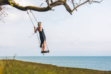 Mature woman balancing on swing in front of sky - OMIF00979