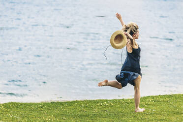 Frau läuft mit Hut genießend vor dem Meer - OMIF00983