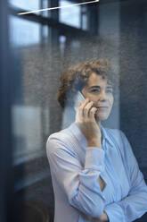 Lächelnde Geschäftsfrau im Gespräch über Smartphone durch Glas gesehen - JOSEF11182