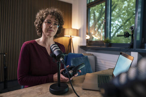 Älterer Moderator mit Brille und Headset sitzt mit Laptop am Schreibtisch in einer Radiostation - JOSEF11220