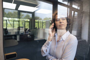 Reife Geschäftsfrau, die mit einem Mobiltelefon spricht, gesehen durch Glas - JOSEF11233