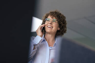 Glückliche Geschäftsfrau mit Brille, die im Büro mit einem Smartphone telefoniert - JOSEF11281