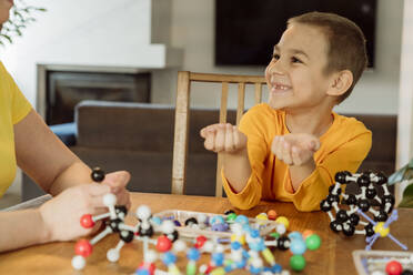 Smiling boy looking at mother by helix model on table - OSF00432