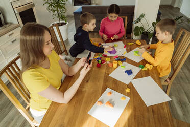 Woman using smart phone by children playing with kinetic sand at home - OSF00441