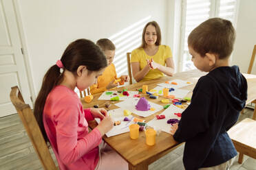 Mutter und Kinder spielen mit kinetischem Sand auf dem Tisch zu Hause - OSF00442