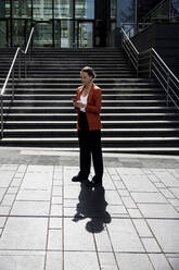 Businesswoman using smart phone on footpath in front of staircase - WPEF06204