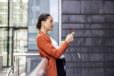 Geschäftsfrau, die ein Smartphone benutzt und sich auf ein Geländer stützt - WPEF06211