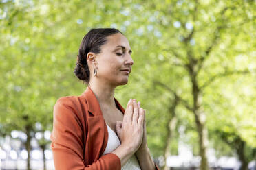 Businesswoman with hands clasped meditating in park - WPEF06229