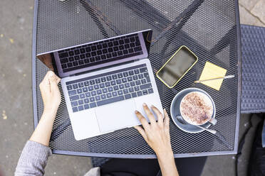 Hände einer Geschäftsfrau, die einen Laptop am Tisch eines Straßencafés benutzt - WPEF06237