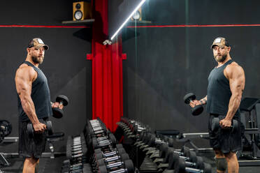 Bodybuilder trainiert mit Hanteln stehend im Fitnessstudio - DLTSF03009